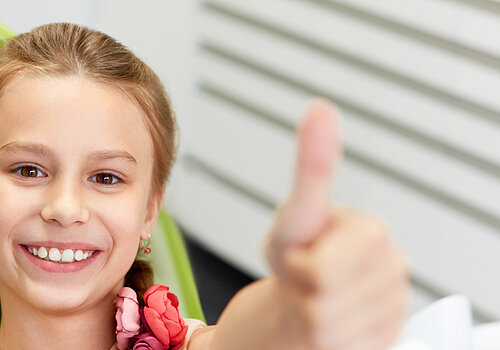 Portrait of happy girl shows thumb up gesture at dental clinic
