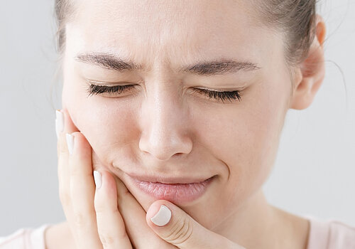 Closeup of beautiful teenage girl isolated on gray background touching her face and closing eyes with expression of horrible suffer from health problem and aching tooth, showing dissatisfaction.